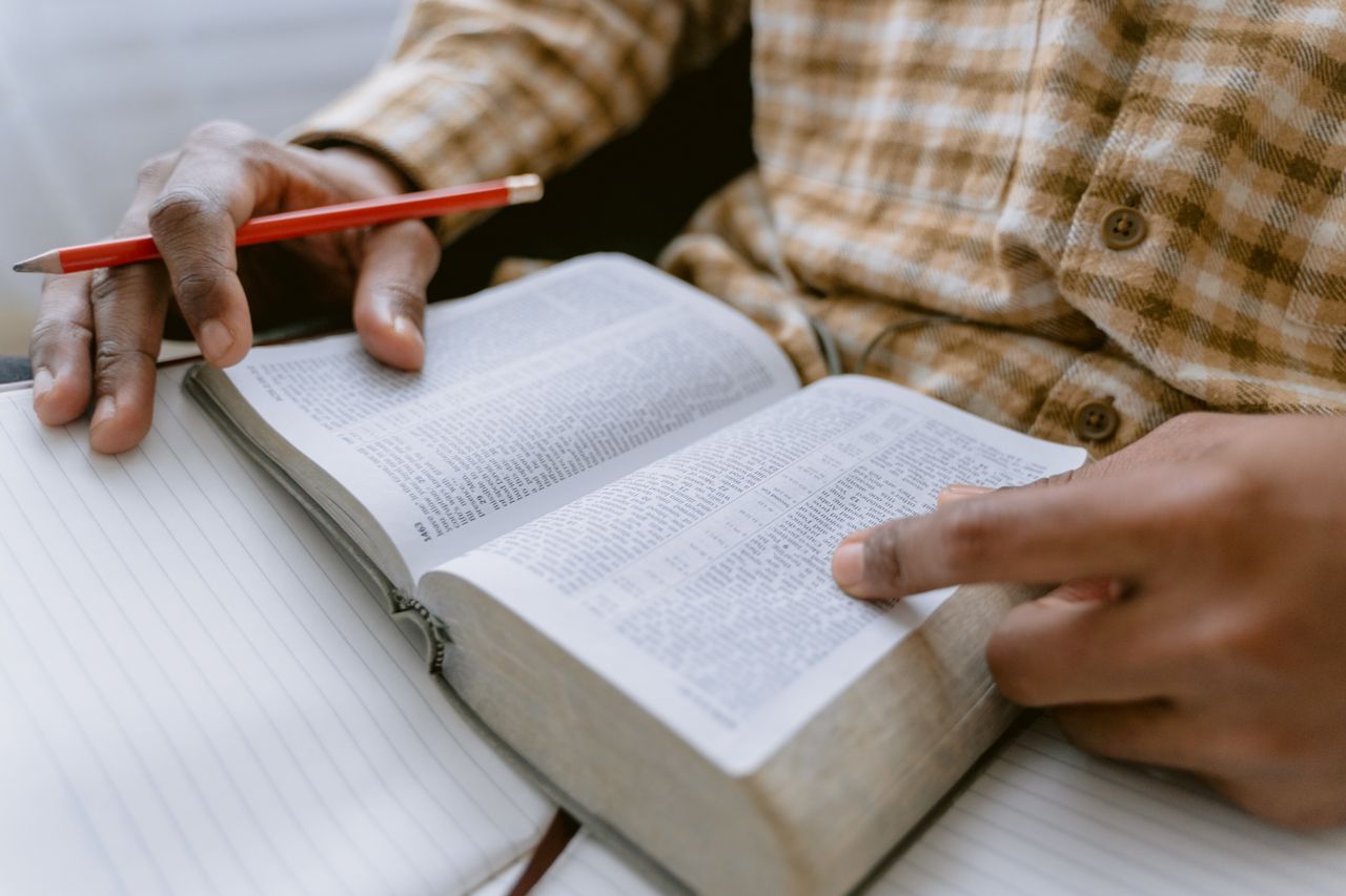 Hands holding an open Bible while taking notes with a pencil.